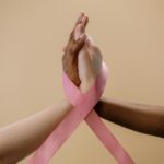 Close-up of hands with a pink ribbon, symbolizing cancer awareness and support.
